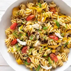 Insalata di pasta con fusilli, pomodorini, zucchine, peperoni gialli e mozzarella fresca. Un piatto colorato e gustoso.