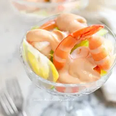 Un delizioso cocktail di gamberi servito in una coppa di vetro, con gamberi succulenti, salsa rosa e una fetta di limone.