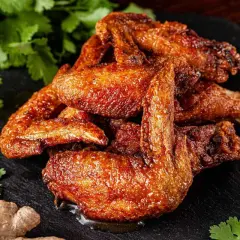 Alette di pollo al forno dorate e succulente, servite su una pietra scura con coriandolo fresco, zenzero e aglio.