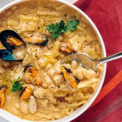 Un cucchiaio raccoglie una porzione di pasta fagioli e cozze, un piatto ricco e saporito, guarnito con prezzemolo fresco.