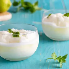 Due bicchieri di sorbetto al limone cremoso, guarniti con menta fresca, su un tavolo di legno blu.