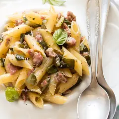 Penne con zucchine e salsiccia, un piatto gustoso e facile da preparare, guarnito con basilico fresco e parmigiano.