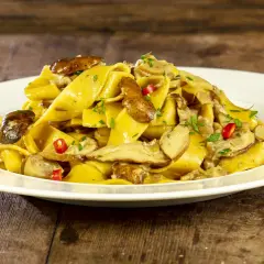 Un piatto invitante di tagliatelle ai funghi porcini, guarnite con peperoncino e prezzemolo fresco, su un tavolo di legno rustico.