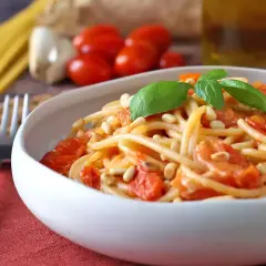 Un piatto invitante di spaghetti con pomodorini freschi, pinoli tostati e basilico, pronto per essere gustato.