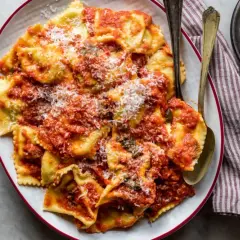 Piatto di tortelli di patate fatti in casa, conditi con sugo rosso e parmigiano grattugiato, pronti per essere gustati.