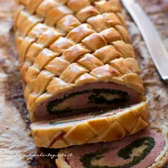Un delizioso polpettone in crosta, con un ripieno di carne, spinaci e formaggio, pronto per essere affettato.