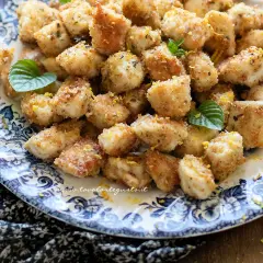 Bocconcini di pollo al forno dorati e croccanti, guarniti con scorza di limone e foglie di menta fresca su un piatto decorato.