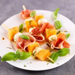 Spiedini di prosciutto e melone con mozzarelline e basilico fresco, un antipasto estivo perfetto.