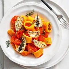 Piatto di pasta con pomodorini e croccanti alici fresche, guarnito con aneto.