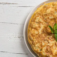 Frittata di cipolle dorata e soffice, guarnita con menta fresca, su un tavolo di legno bianco.