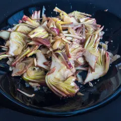 Un piatto nero lucido pieno di un'appetitosa insalata di carciofi crudi, tagliati finemente e conditi.