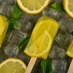 Ghiaccioli al limone con fette di limone e foglie di menta, circondati da cubetti di ghiaccio. Rinfrescante e gustoso.