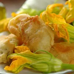 Fiori di zucca in pastella dorati e croccanti, guarniti con i loro stessi fiori freschi.