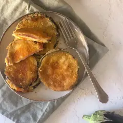 Cordon bleu di melanzane impanati e fritti, ripieni di formaggio filante e prosciutto, serviti su un piatto con una forchetta.