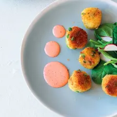 Deliziose polpette di verdure dorate, servite con insalata fresca e salsa rosa su un piatto azzurro.
