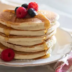 Pancakes senza uova soffici e dorati, inzuppati di sciroppo d'acero e guarniti con frutti di bosco freschi.