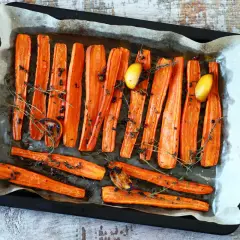 Carote al forno dorate e caramellate, condite con timo fresco, pepe nero e spicchi d'aglio arrostiti, pronte per essere gustate.