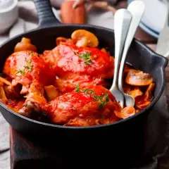 Pollo alla Marengo succulento in padella con funghi e pomodoro, guarnito con timo fresco.