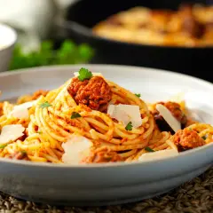 Un piatto invitante di spaghetti con ragù di salsiccia, guarnito con scaglie di parmigiano e prezzemolo fresco.