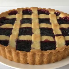 Una crostata di marmellata con una griglia di pasta dorata e un ripieno scuro e invitante.