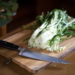 Un coltello affilato pronto a preparare le puntarelle alla romana su un tagliere di legno.