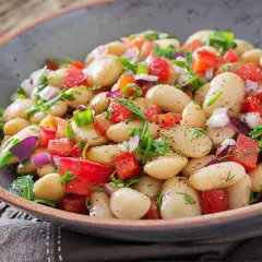 Insalata di fagioli bianchi, pomodori, cipolla rossa e erbe fresche in una ciotola rustica. Un piatto leggero e saporito.