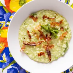 Un cremoso risotto asparagi e speck, guarnito con punte di asparagi freschi e croccanti sfoglie di speck.