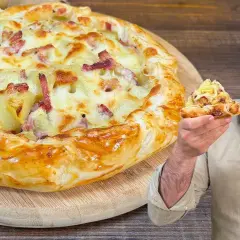 Una golosa torta salata patate e speck, con un uomo che ne mostra una fetta invitante.
