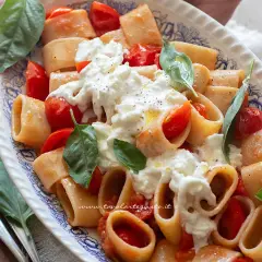 Piatto di pasta con pomodorini e burrata cremosa, guarnito con basilico fresco. Un'esplosione di sapori mediterranei.