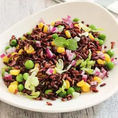 Un colorato riso venere con verdure fresche: piselli, mais, cipolla rossa e lattuga, guarnito con menta.