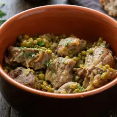 Un saporito agnello con piselli, servito in una ciotola di terracotta, guarnito con prezzemolo fresco.