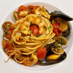 Un piatto invitante di spaghetti allo scoglio, con gamberi, cozze, vongole e calamari, condito con pomodorini e prezzemolo.