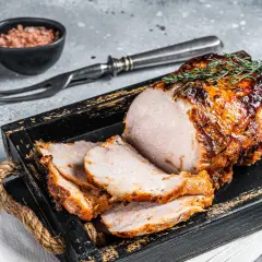 Succulento arrosto di maiale affettato, guarnito con rosmarino, servito su un vassoio di legno scuro con sale rosa e forchettone.