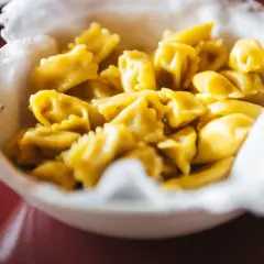 Un primo piatto invitante di ravioli del plin, piccoli e dorati, serviti in una ciotola bordata di bianco.