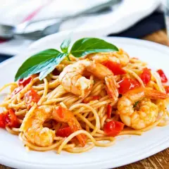 Un piatto invitante di spaghetti con gamberi succulenti e pomodorini freschi, guarnito con basilico.