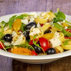 Pasta alla crudaiola con pomodorini, olive nere, rucola e scaglie di parmigiano. Fresca e colorata, un piatto estivo perfetto.