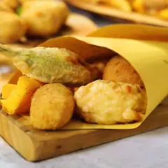 Un cono di carta gialla contiene fritti misti, tra cui spicca una mozzarella in carrozza filante, accompagnata da verdure pastellate e polenta fritta.