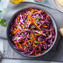 Una fresca insalata di cavolo rosso e carote, guarnita con erbe aromatiche e semi di sesamo, pronta per essere gustata.
