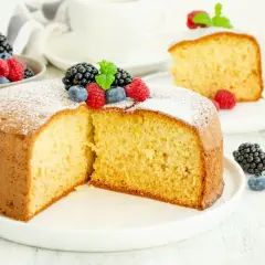 Una soffice torta senza zucchero, spolverata di zucchero a velo e decorata con frutti di bosco freschi, perfetta per una colazione leggera.
