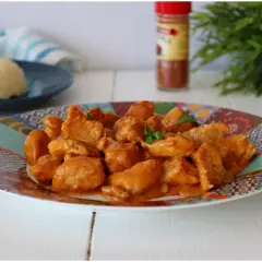 Succulento pollo alla paprika in una salsa cremosa, servito su un piatto colorato con riso bianco sullo sfondo.