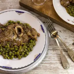 Un piatto di ossobuco con piselli, servito su un tavolo di legno rustico. Le forchette d'argento sono pronte per gustare questa delizia.