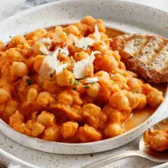 Minestra di ceci cremosa e saporita, guarnita con scaglie di parmigiano e accompagnata da pane tostato.