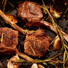 Tre succulenti costolette di agnello in padella, condite con rosmarino e aglio, pronte per essere gustate.