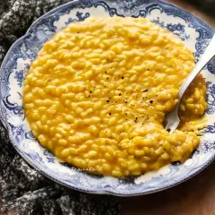 Un invitante risotto con la zucca cremoso, guarnito con pepe nero, su un piatto decorato con un motivo blu e bianco.
