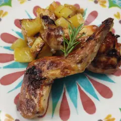 Roasted rabbit pieces with golden potatoes and a rosemary sprig on a colorful floral plate.