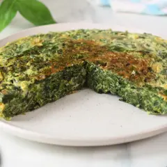Frittata di spinaci dorata e soffice, tagliata a spicchi su un piatto bianco. Un piatto semplice e gustoso.