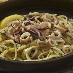 Un piatto invitante di pasta con calamari, guarnito con prezzemolo fresco e una fetta di limone.