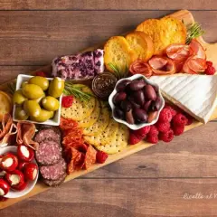 Un invitante tagliere salumi e formaggi con olive, lamponi, pane tostato e peperoncini ripieni.