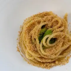 Un piatto di pasta alla carrettiera, spaghetti conditi con mollica tostata e verdure verdi, serviti su un piatto bianco.