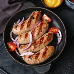 Salsiccia in padella, grigliata e succulenta, servita con pomodorini e cipolla rossa. Un piatto invitante pronto per essere gustato.